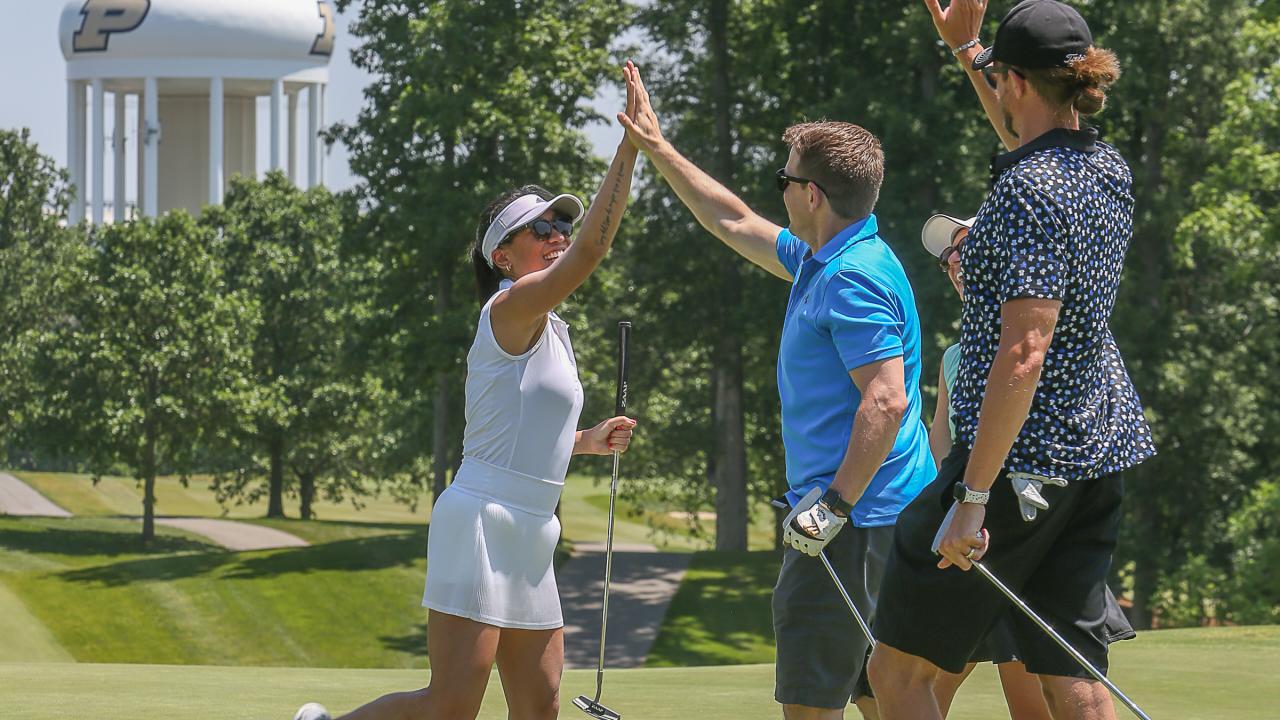 A female golfer in a white golf outfit high-fives a male golfer in a blue shirt and a male golfer in a gray shirt.