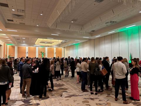 Hundreds of people gather in a hotel ballroom for a professional networking reception.