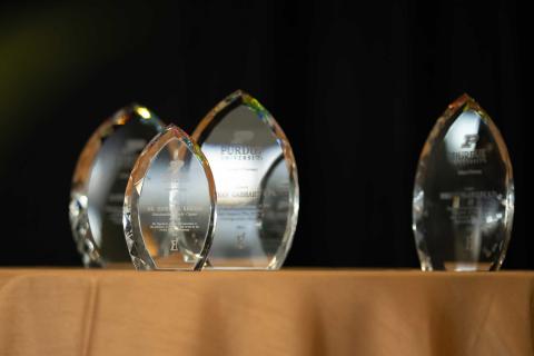 Four glass awards trophies sit on a gold-clothed table with a black backdrop.