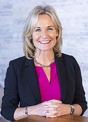 Headshot of a blonde-haired white woman in a pink blouse and black blazer.