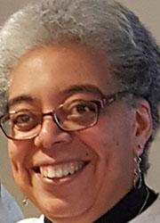 Headshot of a gray-haired black woman with glasses wearing a white shirt with black turtle neck.