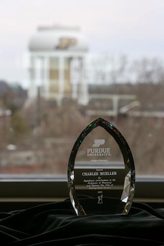 A clear crystal trophy sits atop a black tablecloth in front of the Purdue water tower.