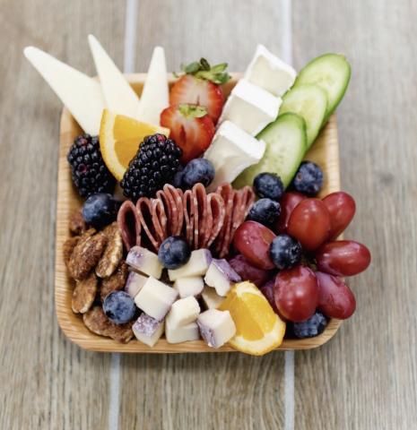 A charcuterie board with grapes, oranges, pretzels, cheeses, cucumbers, and blueberries.