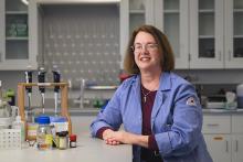 Female scientist leans on a pharmaceutical lab bench.